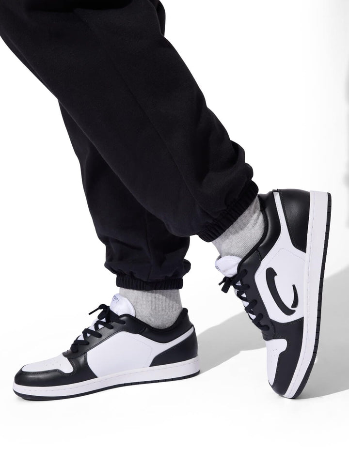 Black and white sneakers worn with black pants on a white background