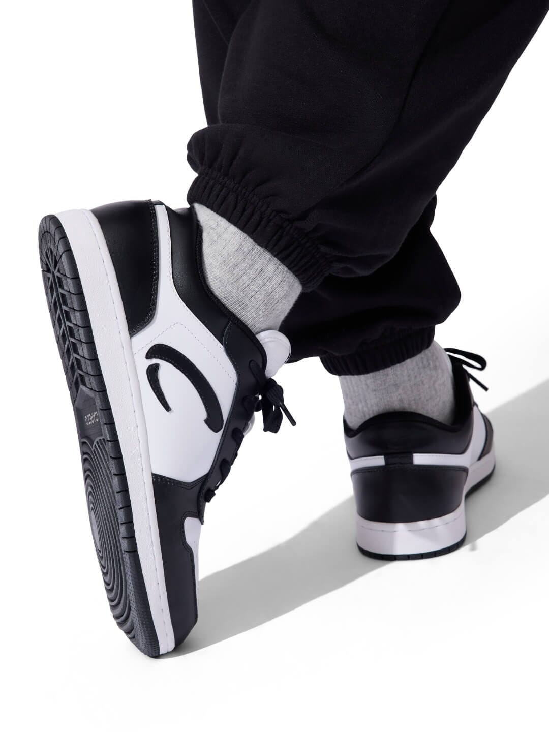 Black and white sneakers worn with black pants on a white background