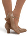 Brown heeled shoes with a bow detail worn by a person on a white background
