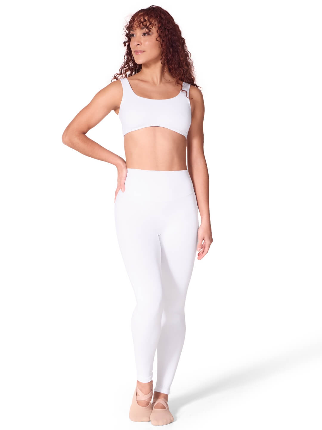 Woman wearing a white sports bra and leggings on a white background