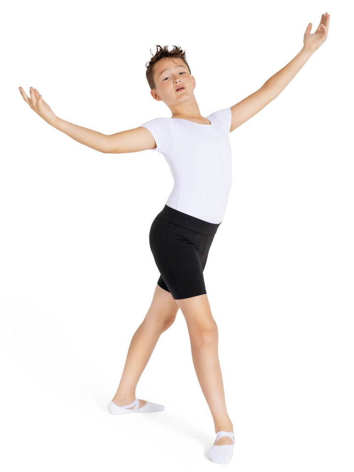 Child in a white top and black shorts with arms outstretched on a white background