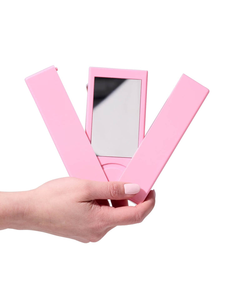 Hand holding a pink folding mirror on a white background