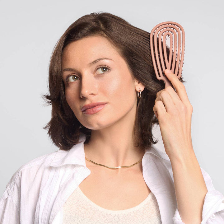 Woman holding a rose gold hairbrush against a light gray background