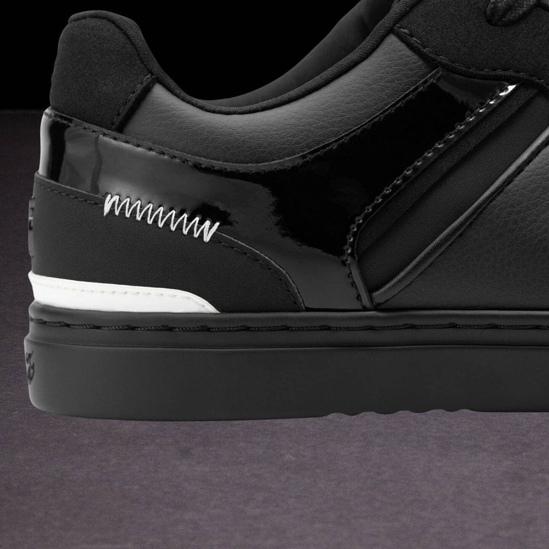 Close-up of a black sneaker with white stitching on a dark background