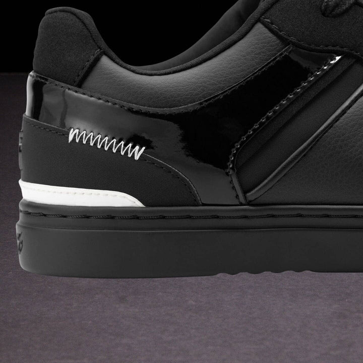Close-up of a black sneaker with white stitching on a dark background