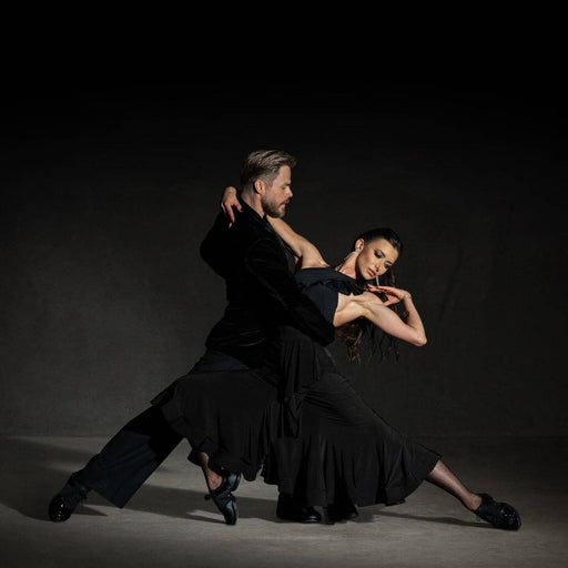 Two dancers in black attire performing a dramatic pose against a dark background