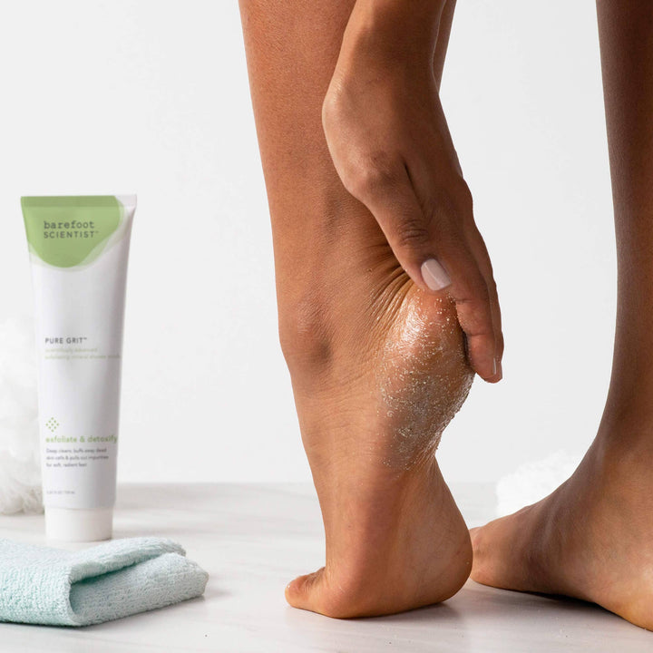 Person applying foot cream to their heel with a tube of 'barefoot scientist' cream and towel in the background.