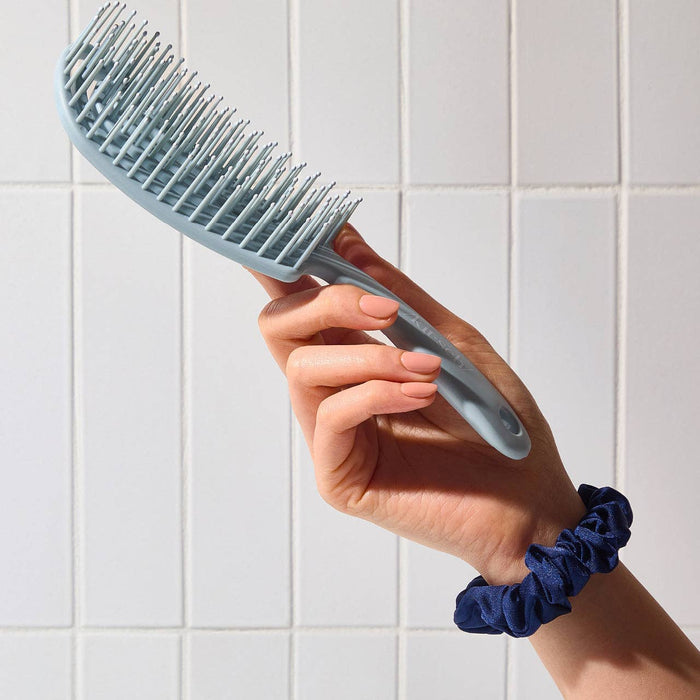 Hand holding a blue pet grooming brush against a tiled wall background