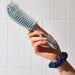 Hand holding a blue pet grooming brush against a tiled wall background