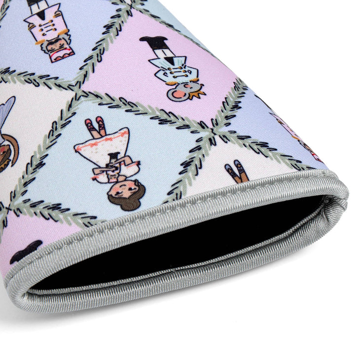 A close-up of a rolled fabric item, likely a blanket or cushion cover, featuring a whimsical cartoon pattern of characters inside pastel diamond-shaped panels outlined with green pine branches. The fabric has a light blue and pink background with gray ribbed edges.