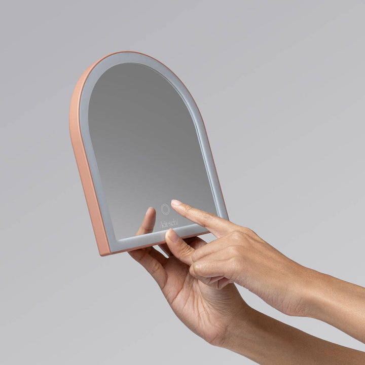 Hand holding a light-up makeup mirror with a gray background