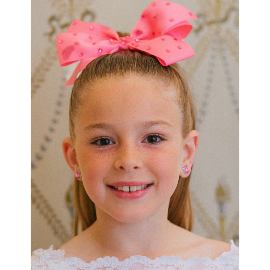 Young girl with a large pink bow in her hair, wearing matching earrings.