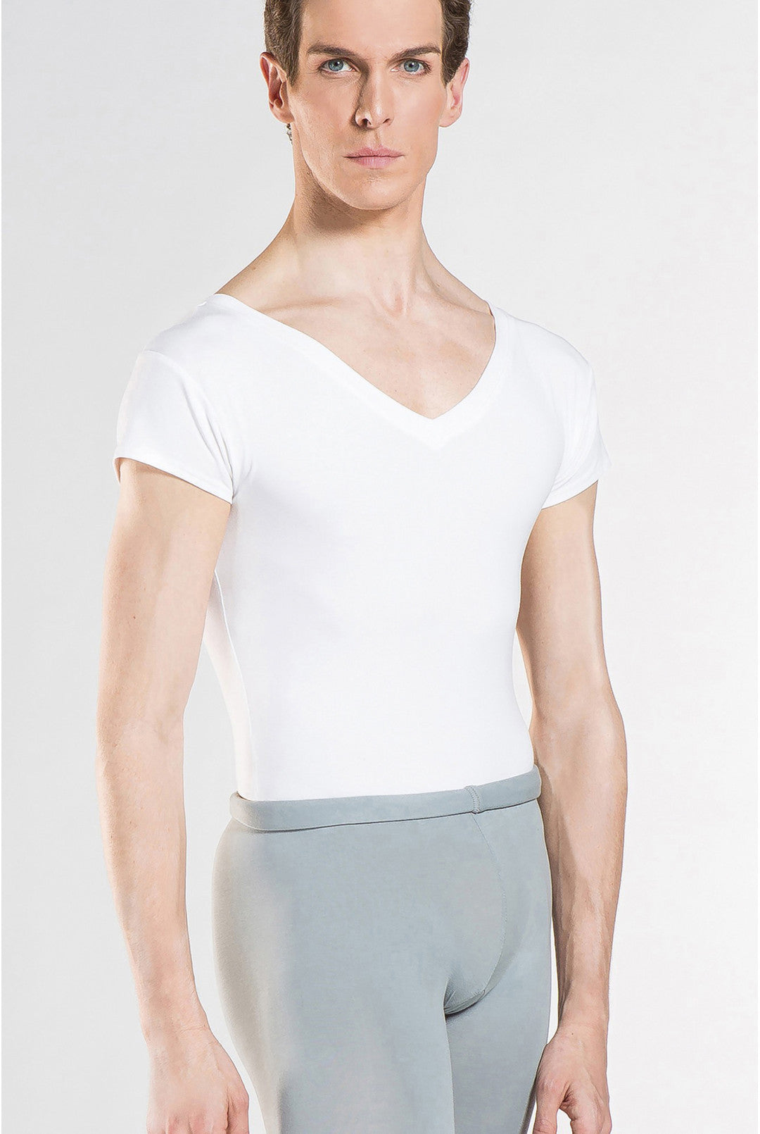 A male model wearing a white short-sleeve V-neck leotard and light gray dance tights, photographed against a clean light gray studio background.