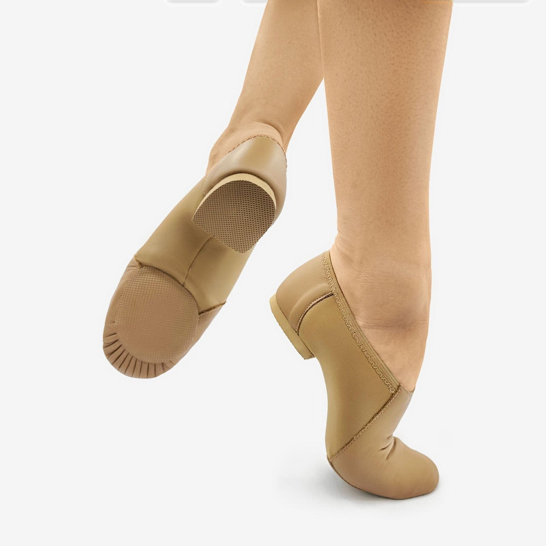 Tan ballet shoes worn with beige tights on a white background