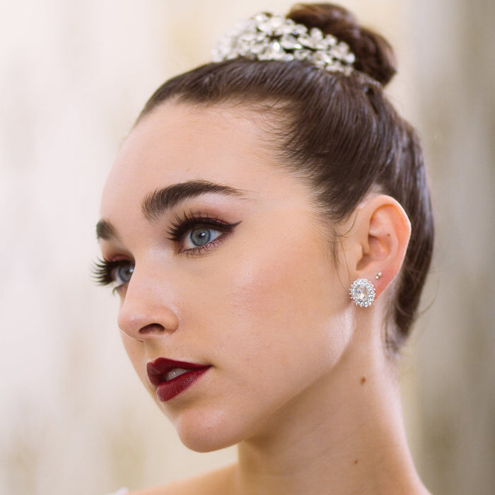 Close-up of a woman with elegant hair and makeup, wearing a decorative headband and earrings.
