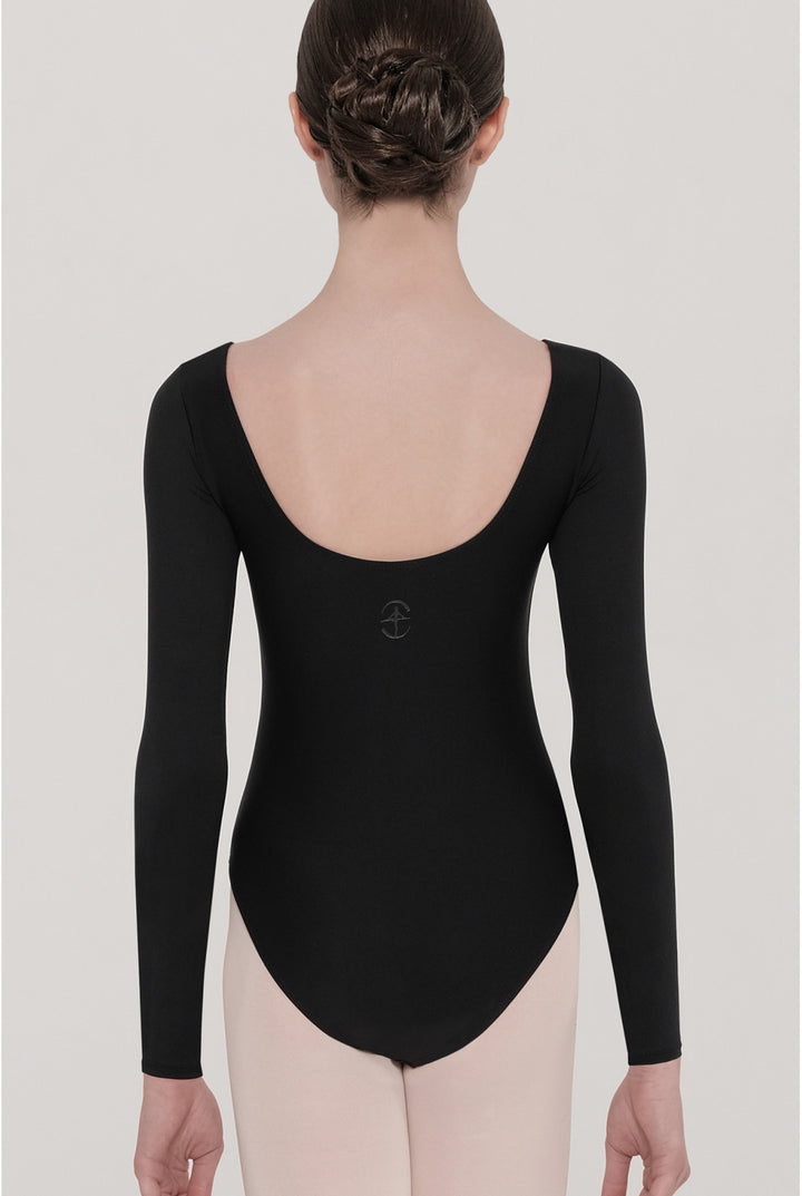 A model shown from the back wearing a black long-sleeve leotard with a wide scoop neckline and a small dark logo centered on the upper back, paired with light pink tights against a light gray studio background.