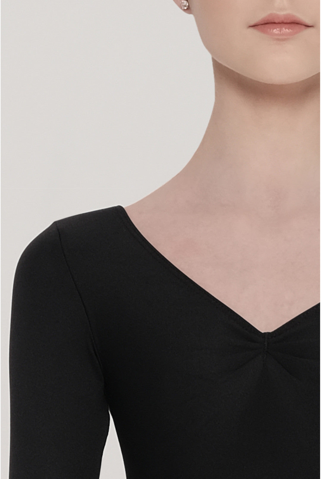 Close-up of a person wearing a black long-sleeve top with a V-neckline on a plain background.