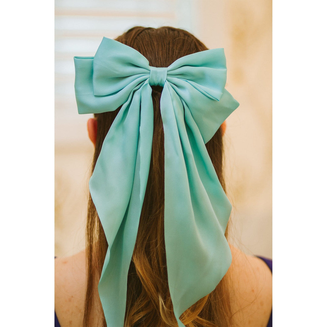 Person wearing a large turquoise hair bow with a plain background