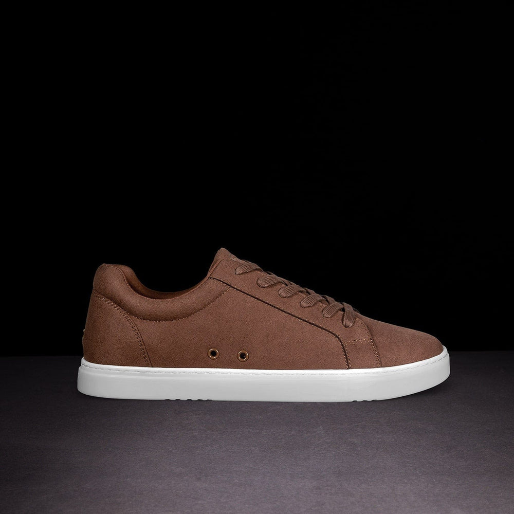 Brown sneaker with white sole on a dark background