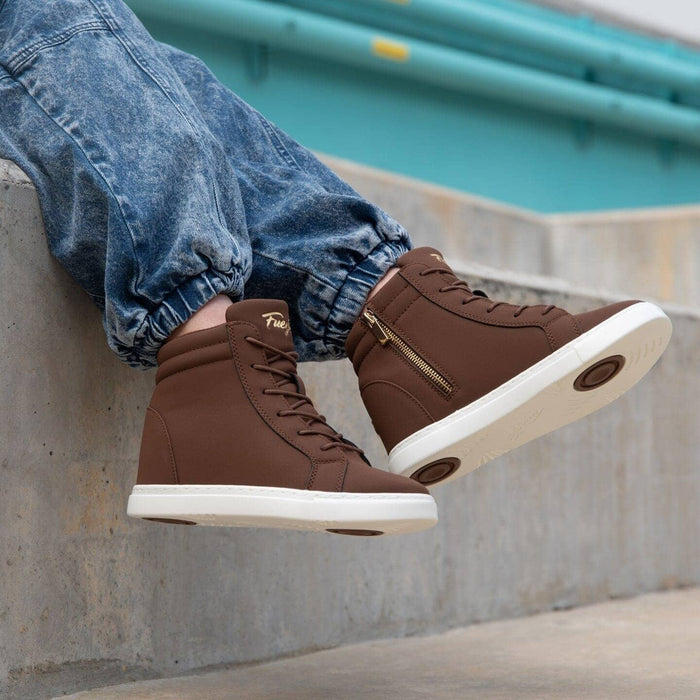 Brown high-top sneakers with white soles worn by a person sitting on a concrete ledge.