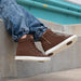 Brown high-top sneakers with white soles worn by a person sitting on a concrete ledge.