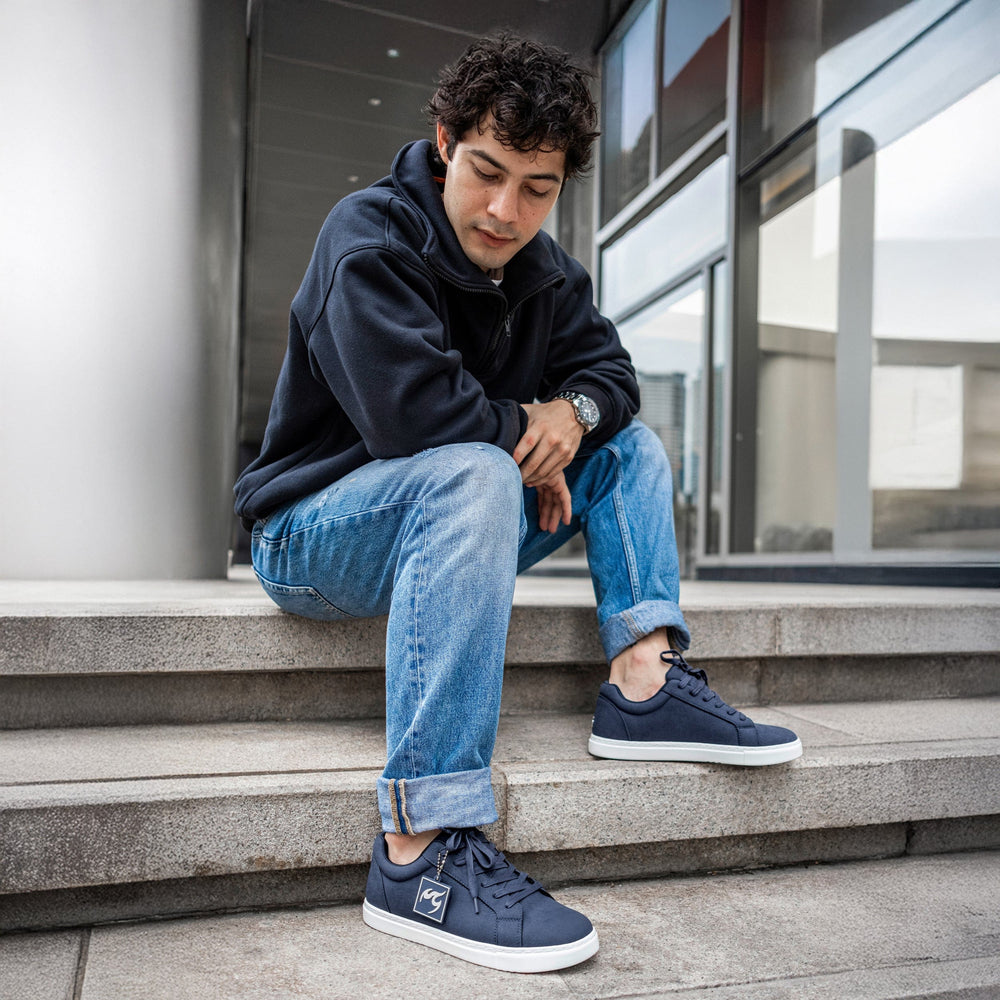 Person wearing navy blue sneakers sitting on steps outside a modern building.