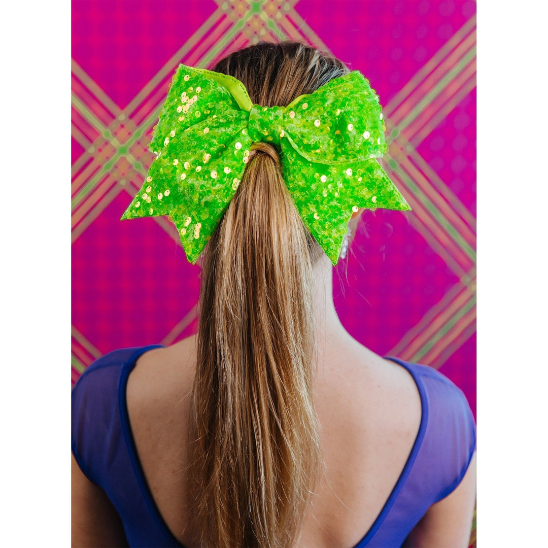 Person wearing a large green sequin bow in their hair against a pink and green checkered background