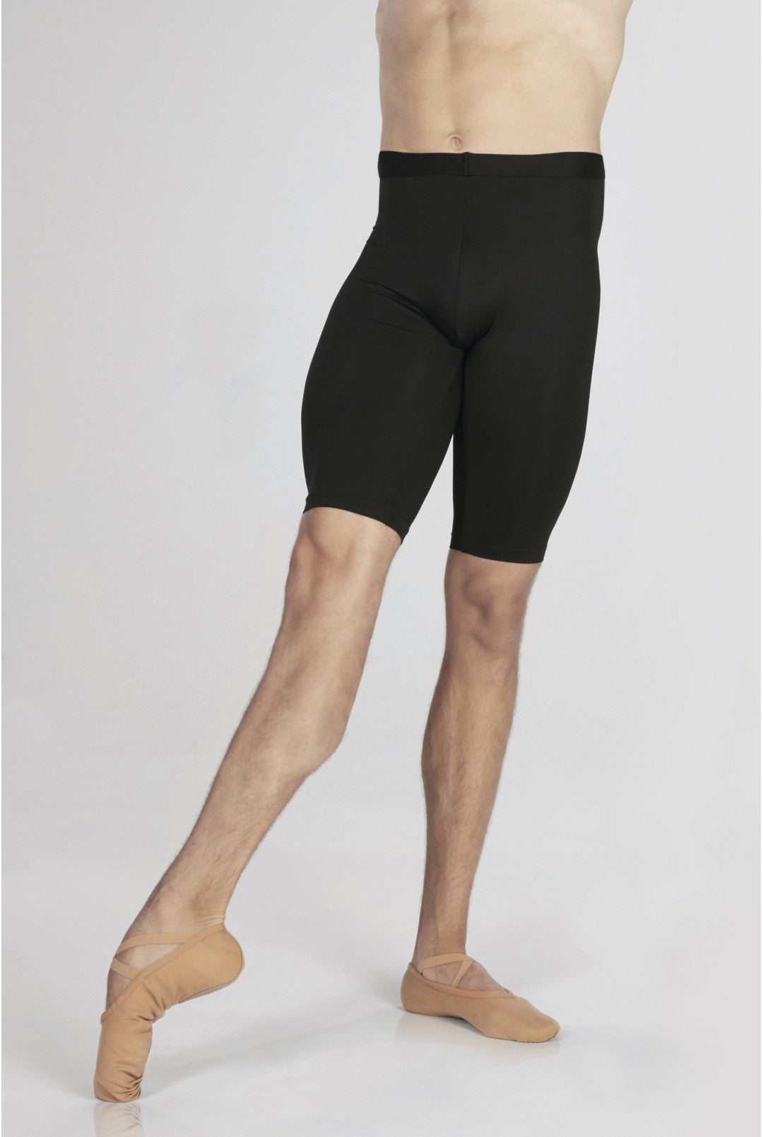 Person wearing black ballet shorts and beige ballet shoes on a white background