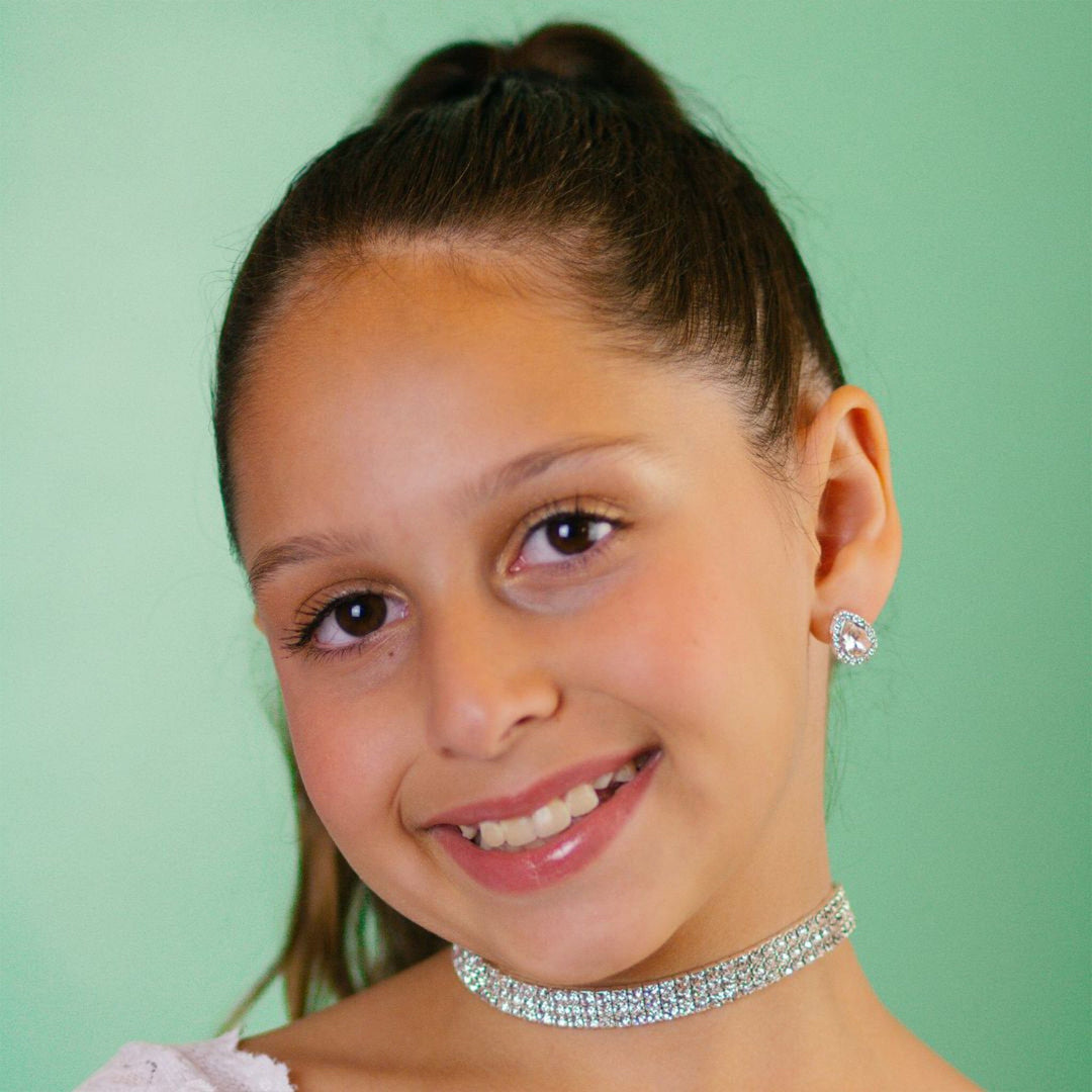 Young girl wearing a sparkling necklace and earrings against a green background