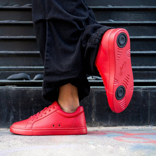 Red sneakers worn with black pants on a black metal staircase.