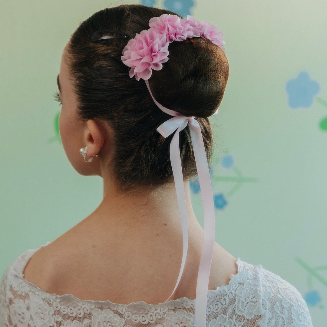 Woman with a bun hairstyle decorated with pink flowers and ribbons against a light green background