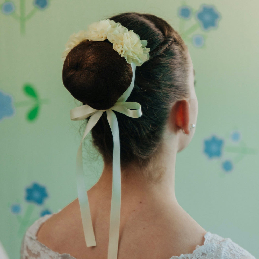 Person with hair styled in an updo with a flower and ribbon, against a floral-patterned background.