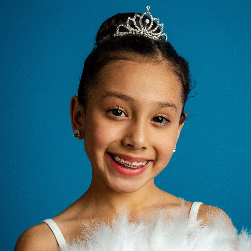 Young girl wearing a tiara and feathered garment against a blue background