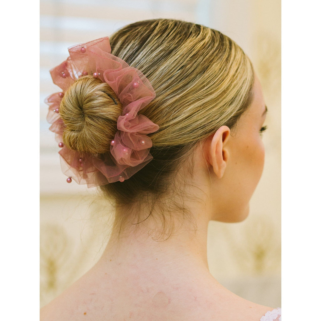 Woman with a bun adorned with a pink sheer hair accessory against a neutral background