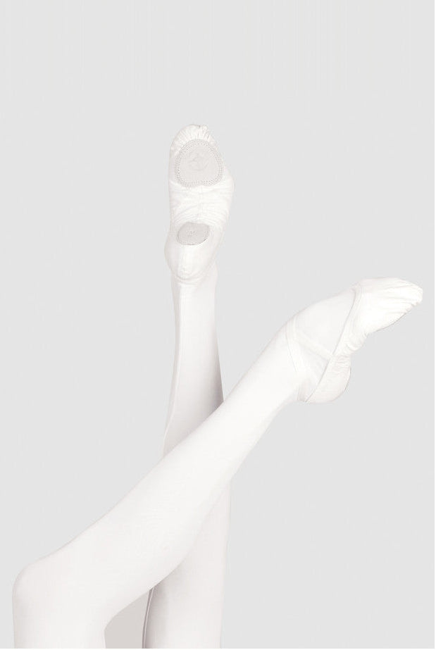 White ballet pointe shoes worn on crossed legs, shown against a light gray studio background.